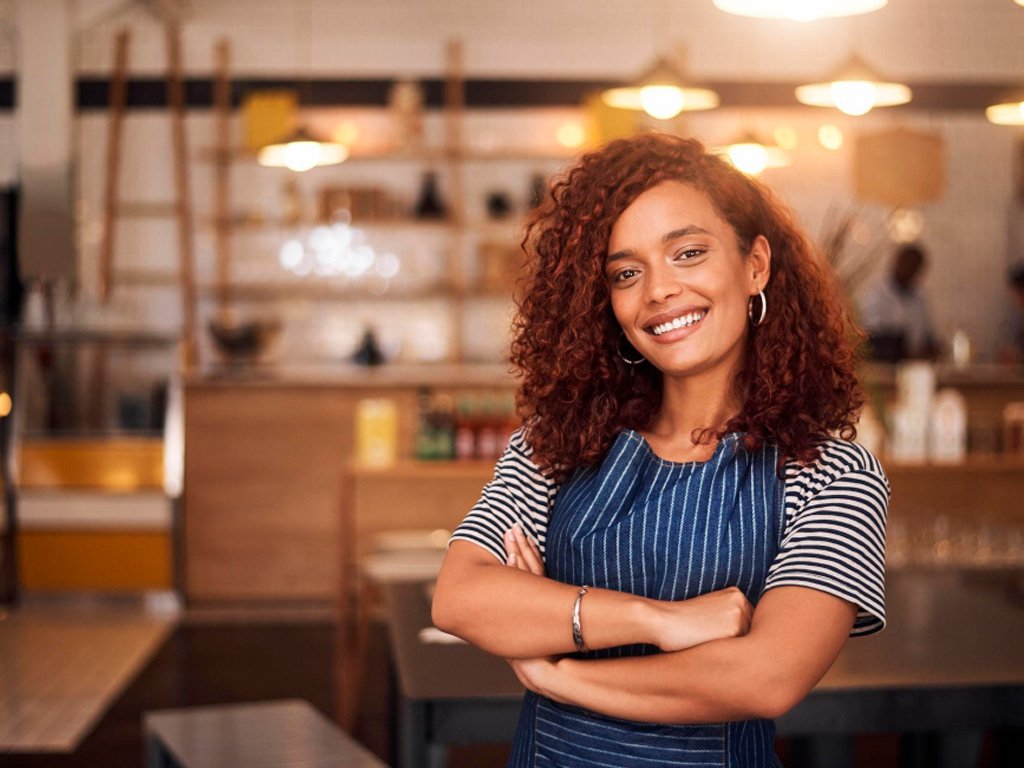 Empreendedora sorrindo em ambiente comercial representando informações e obrigações do MEI 2026