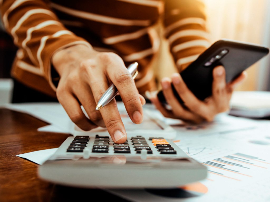 Profissional utilizando calculadora e celular analisando impostos para redução tributária legal para empresas