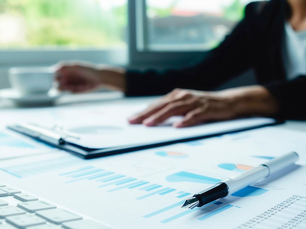 Profissional analisando relatórios financeiros e contábeis com gráficos, planilhas e documentos sobre a mesa.